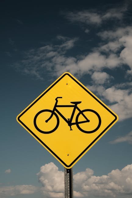 Yellow bicycle warning sign on a pole against a cloudy blue sky.